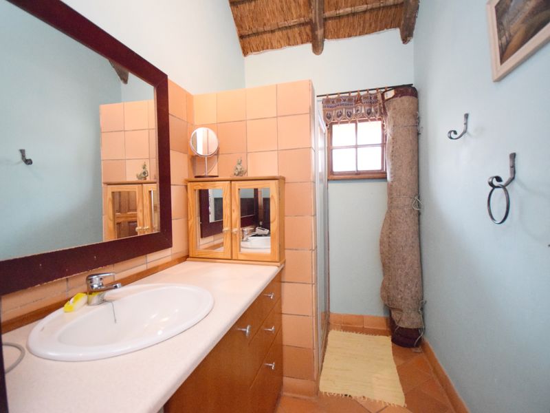 A bathroom featuring a vanity with a basin, tiled splashback, shower enclosure, and a traditional thatched roof ceiling.