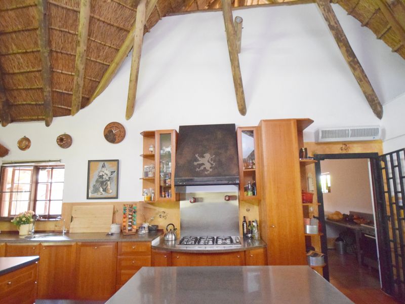 A rustic kitchen featuring a high thatched ceiling with exposed timber rafters, wooden cabinetry, a gas hob with extractor, and an adjoining scullery area.