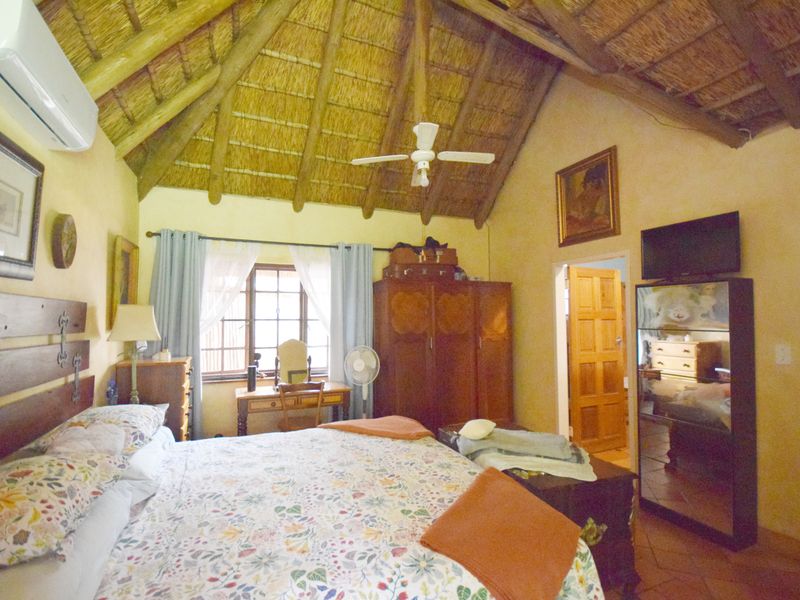 A spacious bedroom featuring a high vaulted thatched ceiling with exposed timber rafters, tiled flooring, and a wall-mounted air conditioning unit.