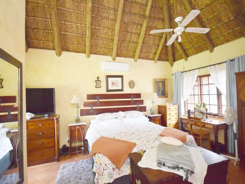 A cozy bedroom featuring a traditional thatched roof with exposed timber rafters, tiled flooring, and a split-system air conditioner for climate control.