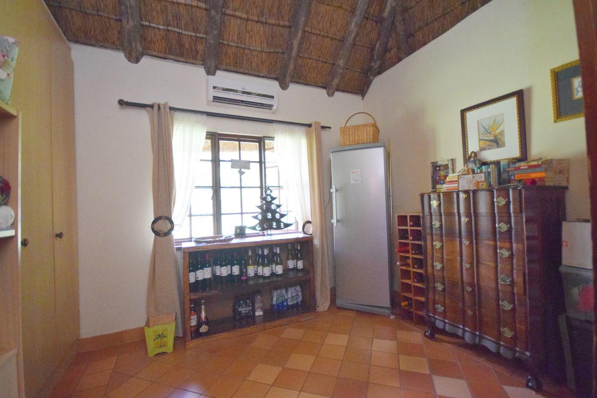 A bedroom featuring a traditional thatched roof with exposed timber rafters, terracotta floor tiles, and a built-in wardrobe.