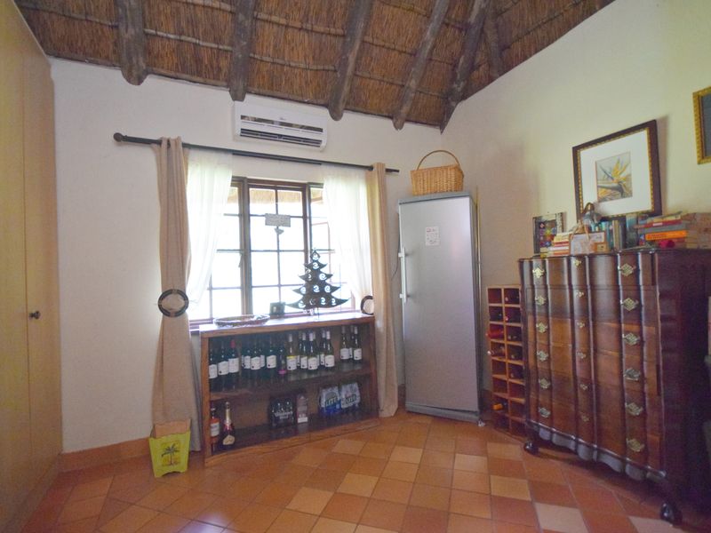 A bedroom featuring a traditional thatched roof with exposed timber rafters, terracotta floor tiles, and a built-in wardrobe.