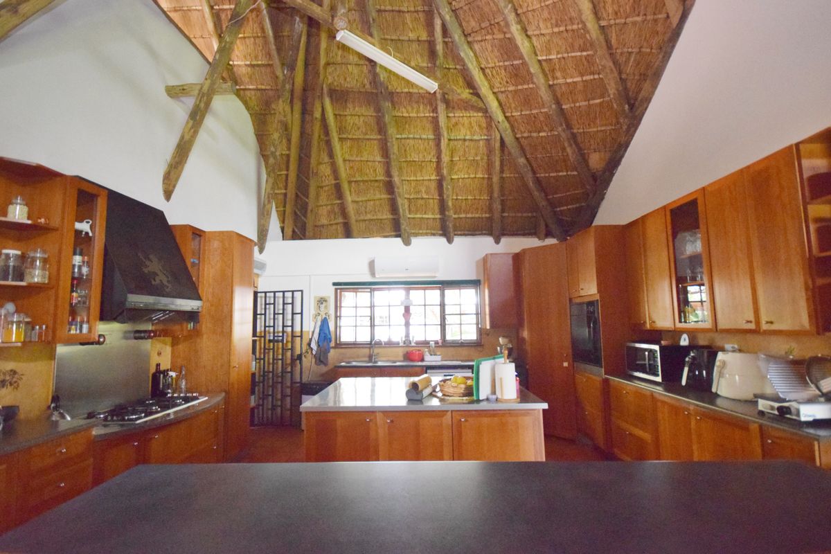 Spacious kitchen featuring a high vaulted thatched ceiling with exposed timber rafters, wooden cabinetry, a central island, and integrated appliances.