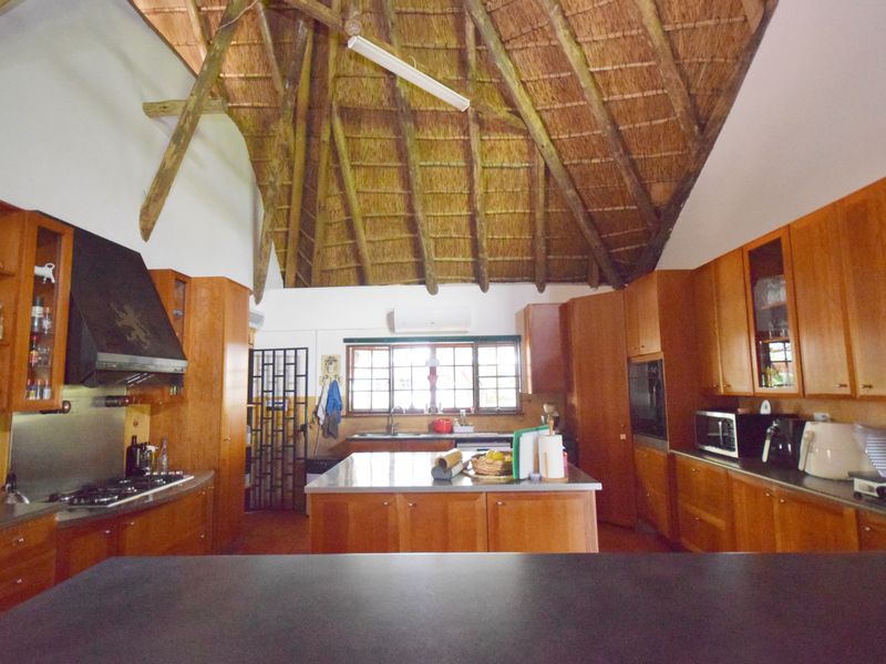 Spacious kitchen featuring a high vaulted thatched ceiling with exposed timber rafters, wooden cabinetry, a central island, and integrated appliances.