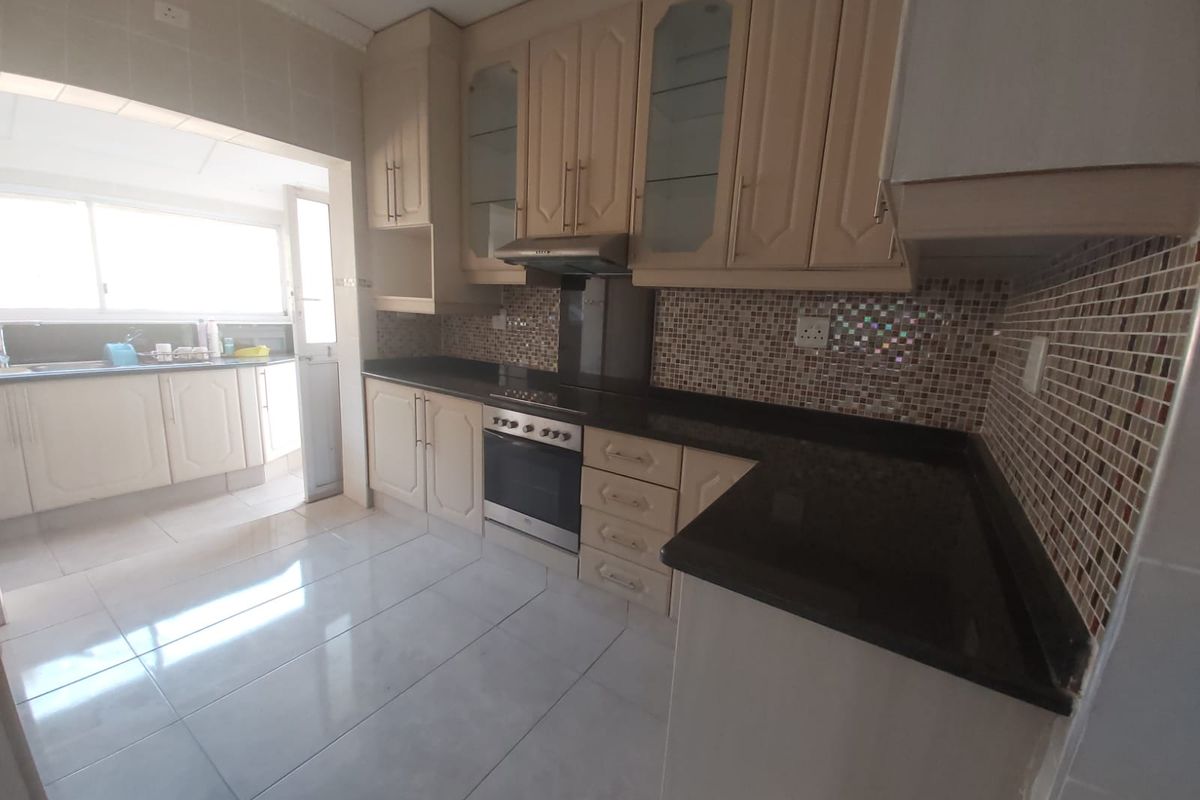 A functional kitchen featuring built-in cabinetry, granite countertops, a mosaic tile backsplash, and integrated oven with extractor fan.