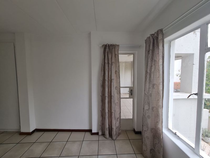An empty living area featuring neutral tiled flooring, large windows for natural light, and direct access to an outdoor balcony space.