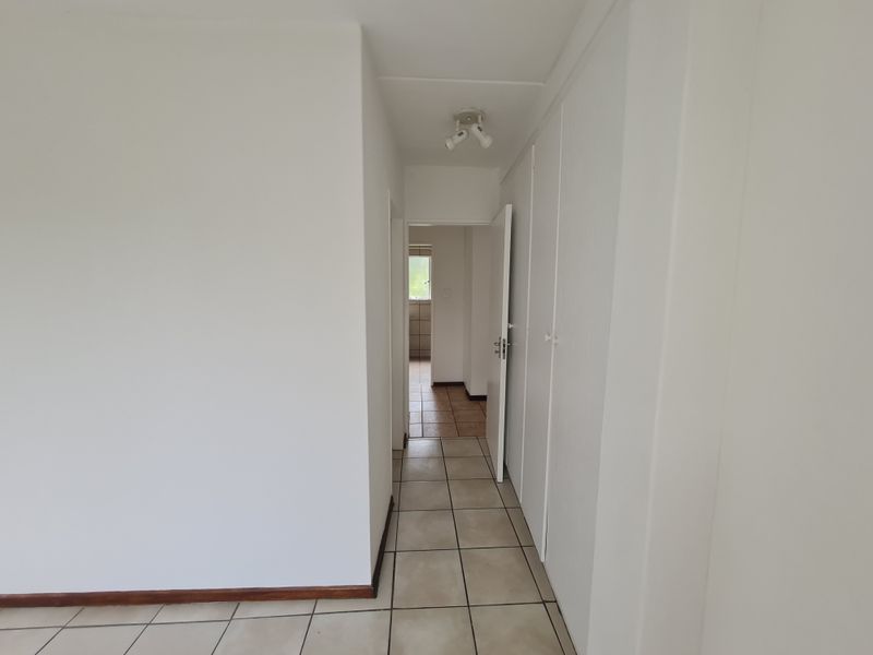A clean, neutral hallway featuring tiled flooring and built-in storage cupboards, providing access to adjacent rooms within the apartment.