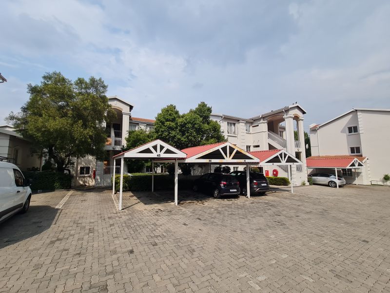 Exterior view of an apartment complex featuring paved parking areas and covered carport structures with building access via external staircases.
