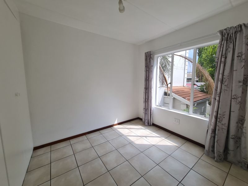 A bright, empty bedroom featuring neutral tiled flooring, a built-in cupboard, and a large window providing natural light.