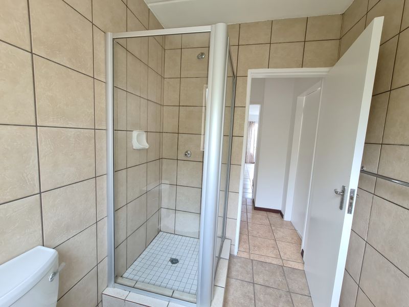 A functional bathroom featuring a glass-enclosed shower, tiled walls and flooring, and a standard toilet, presenting a clean and neutral space.