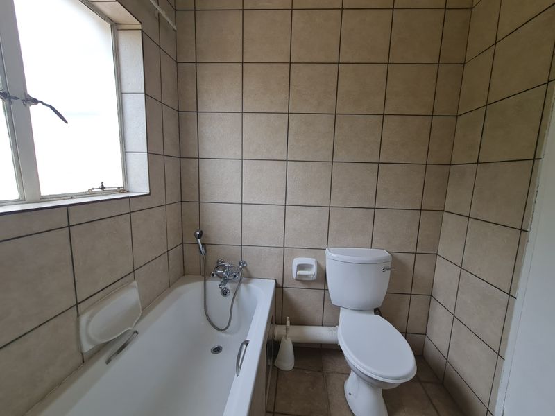 A functional bathroom featuring a bathtub with a handheld shower mixer, a standard toilet, and full-height wall tiling.