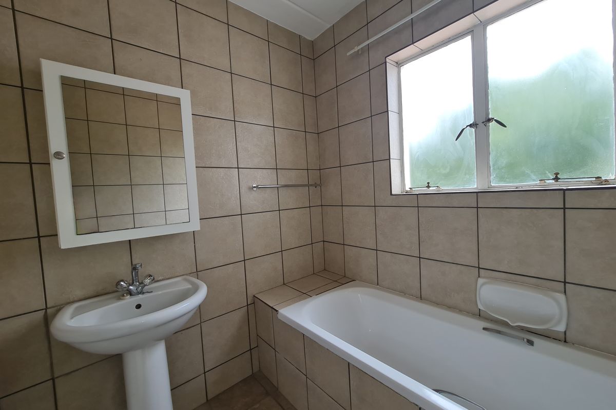 A functional bathroom featuring a pedestal basin, bathtub, and neutral wall tiling, offering a clean canvas for potential modern updates.