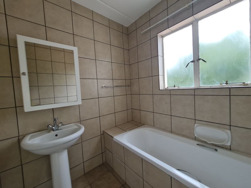 A functional bathroom featuring a pedestal basin, bathtub, and neutral wall tiling, offering a clean canvas for potential modern updates.