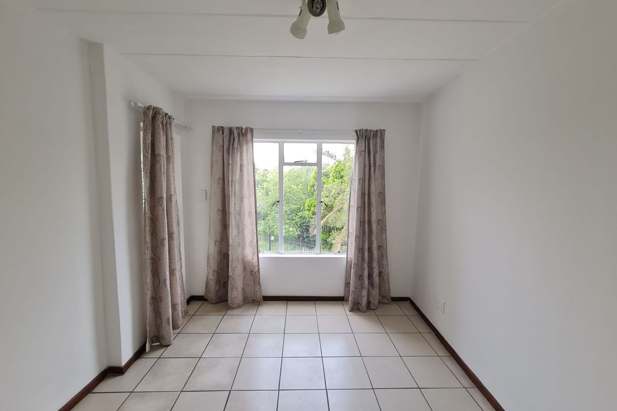 A bright, empty living area featuring neutral tiled flooring and a large window with garden views, providing a blank canvas for interior design.