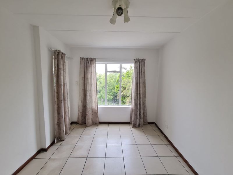 A bright, empty living area featuring neutral tiled flooring and a large window with garden views, providing a blank canvas for interior design.