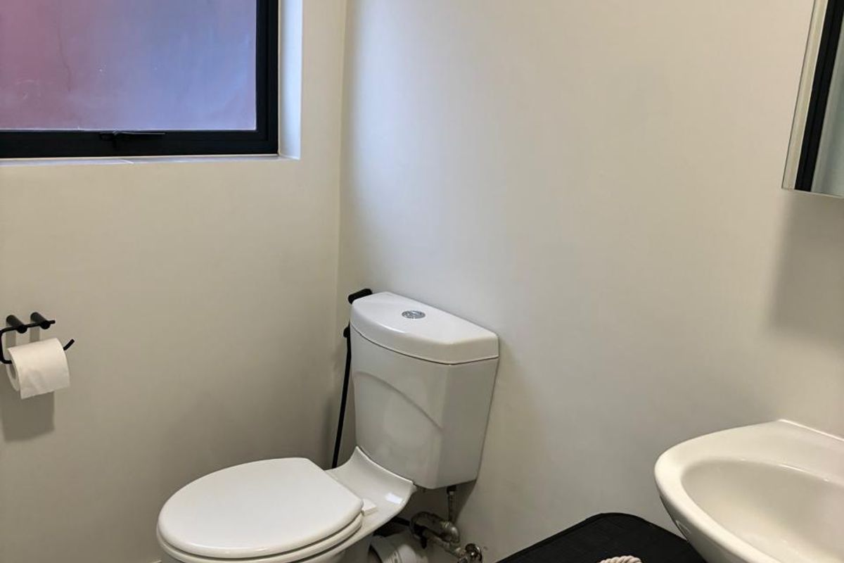 A compact guest bathroom featuring a white pedestal basin, a standard toilet, and a window with a modern black frame.