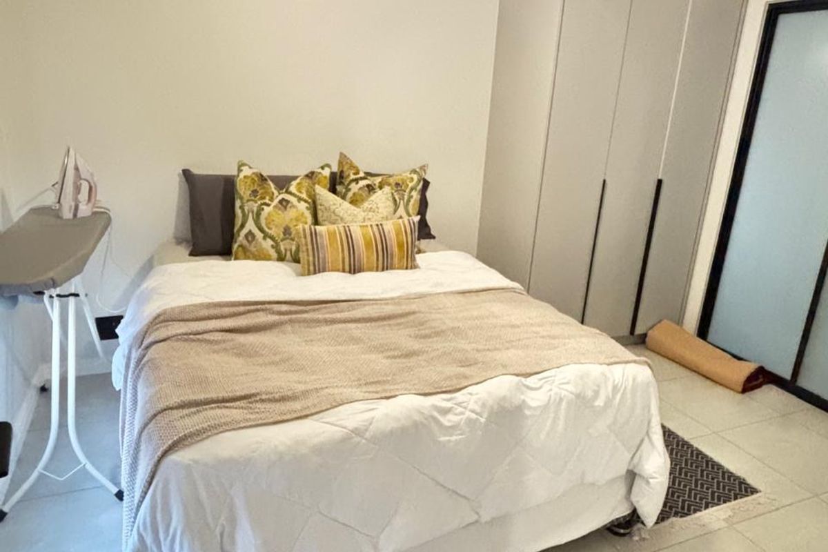 A well-maintained bedroom featuring neutral tiled flooring, a built-in wardrobe, and a modern pendant light fixture.