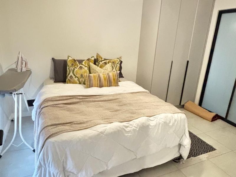 A well-maintained bedroom featuring neutral tiled flooring, a built-in wardrobe, and a modern pendant light fixture.