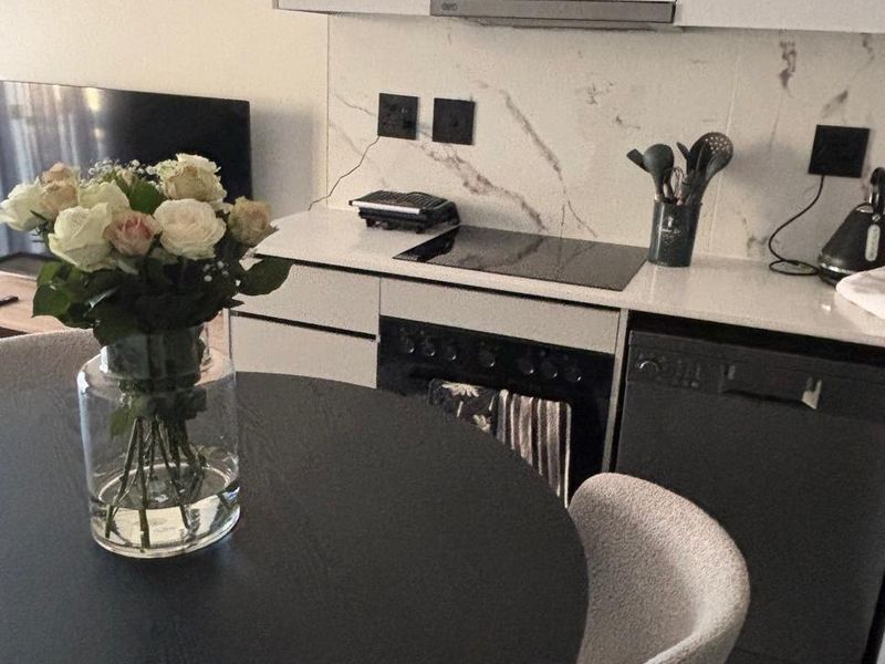 Modern open-plan kitchen featuring sleek white cabinetry, marble-look splashback, stone countertops, and integrated appliances, seamlessly flowing into the dining area.