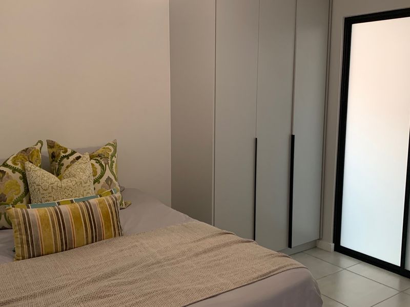 A well-maintained bedroom featuring modern built-in wardrobes, neutral tiled flooring, and a frosted glass door providing natural light.
