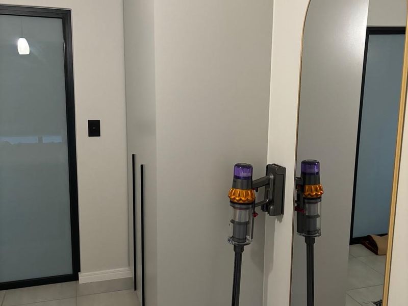 A modern bedroom interior featuring a sleek built-in wardrobe, neutral tiled flooring, and a contemporary arched wall mirror.
