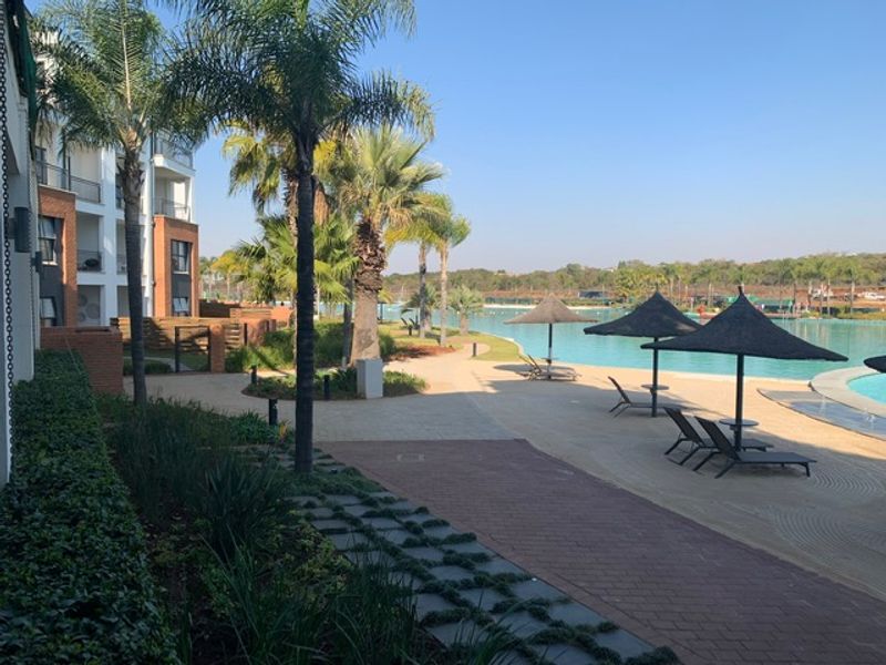 A well-maintained communal pool area featuring paved walkways, landscaped gardens, and direct access to the apartment building exterior.