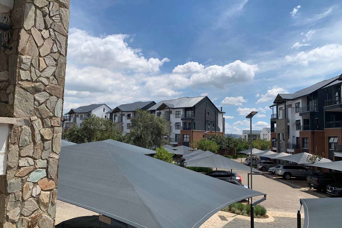 View of the apartment complex exterior featuring stone cladding, paved parking areas, and functional shade cloth carports under a clear sky.