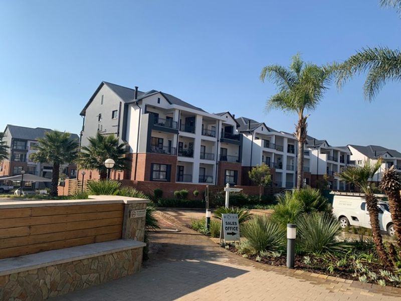 A view of a modern multi-story apartment complex featuring brick and white facade finishes, balconies, and well-maintained landscaped grounds.