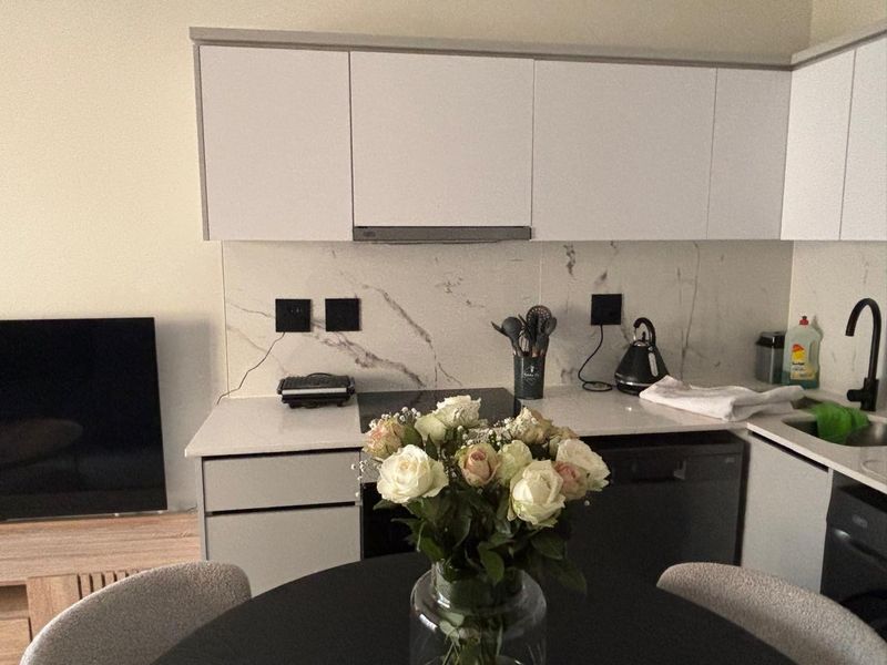 Modern open-plan kitchen featuring sleek white cabinetry, marble-look splashback, and high-quality fixtures, seamlessly integrated into the living space.