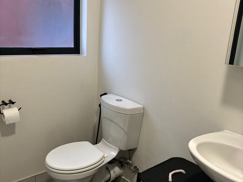 A functional bathroom featuring a white toilet, pedestal basin, and tiled flooring with a window providing natural light.