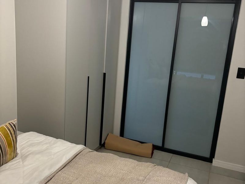 A modern bedroom featuring neutral tones, tiled flooring, a built-in wardrobe, and a sleek sliding glass door providing access to the space.