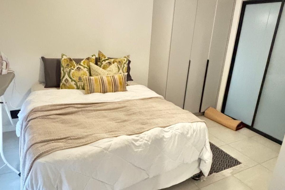 A well-maintained bedroom featuring neutral tiled flooring, a built-in wardrobe, and a modern pendant light fixture.