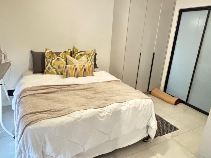 A well-maintained bedroom featuring neutral tiled flooring, a built-in wardrobe, and a modern pendant light fixture.
