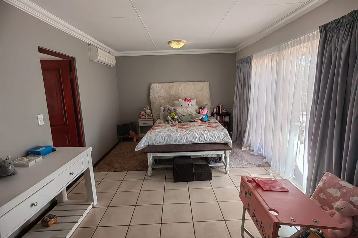 A spacious bedroom featuring tiled flooring, an integrated air conditioning unit, and large sliding glass doors that provide access to the exterior.