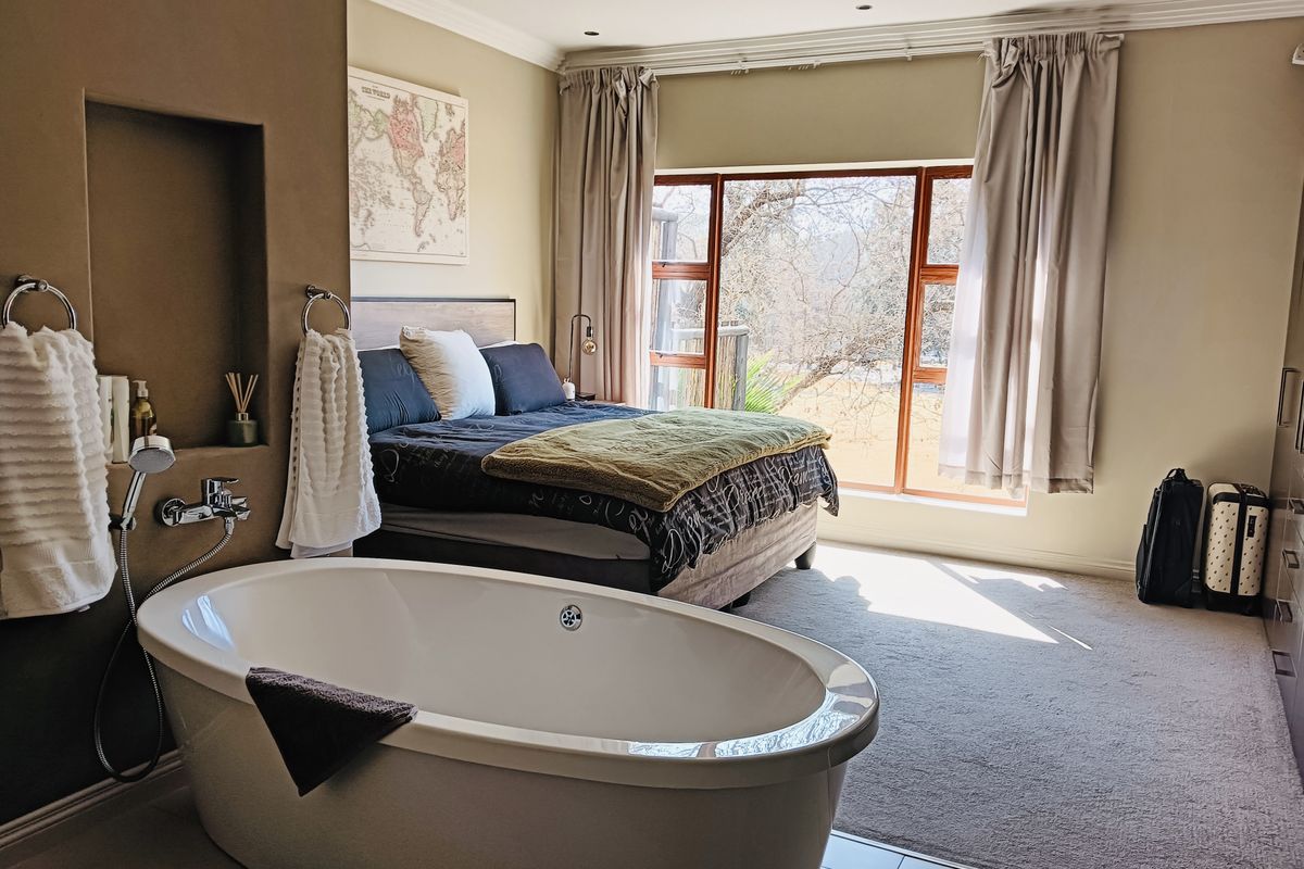 Spacious bedroom featuring an open-plan ensuite with a modern freestanding bathtub, built-in storage, and large windows providing natural light and garden views.