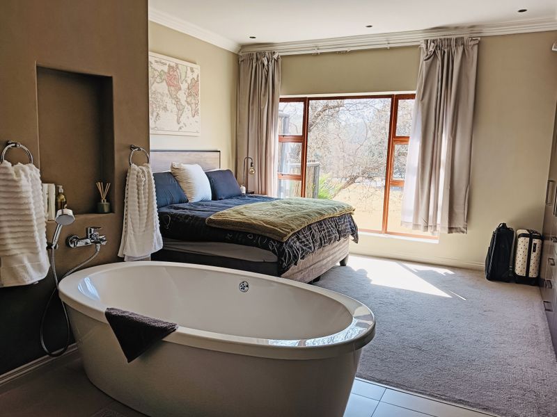Spacious bedroom featuring an open-plan ensuite with a modern freestanding bathtub, built-in storage, and large windows providing natural light and garden views.