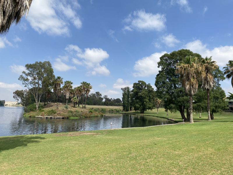 A scenic view of a tranquil lake surrounded by lush green lawns and mature trees, offering a peaceful outdoor setting.