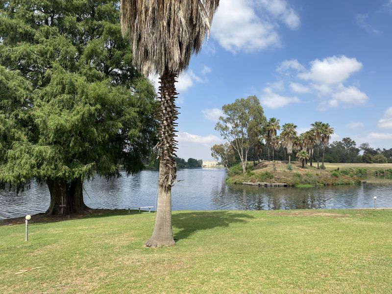 A scenic view of a tranquil lake surrounded by mature trees and well-maintained lawn, offering a peaceful outdoor setting.