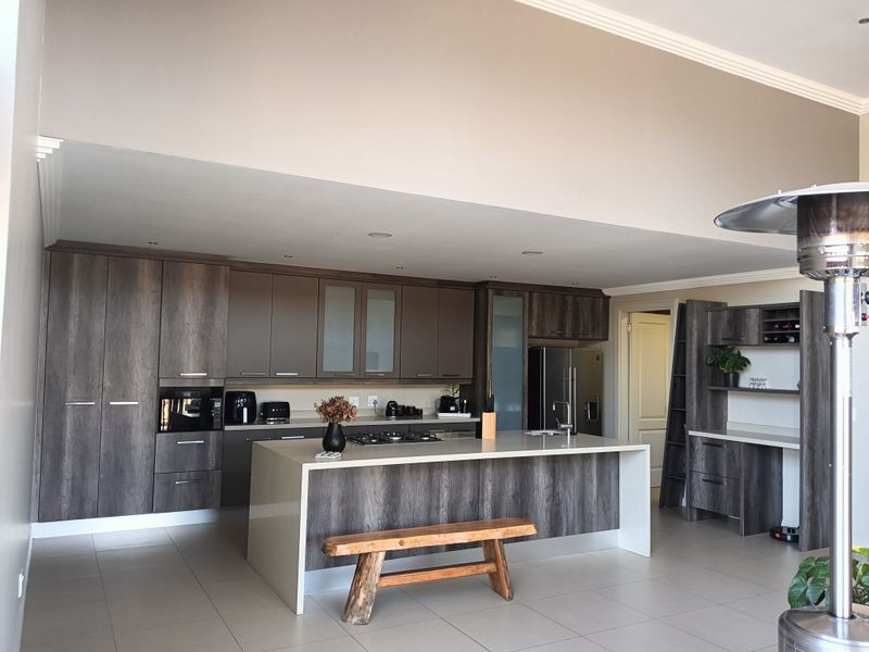 Modern kitchen featuring dark wood-grain cabinetry, a large central island with stone countertops, integrated appliances, and sleek tiled flooring.
