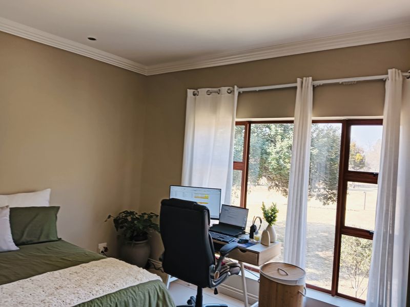A bedroom featuring crown molding, large windows providing natural light, and tiled flooring, currently utilized as a combined sleeping and workspace area.