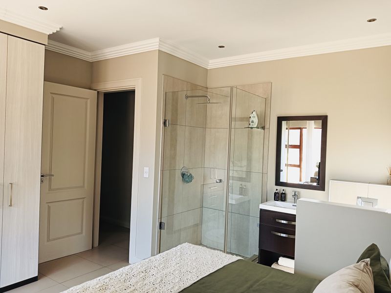 A modern bedroom featuring an integrated en-suite bathroom with a glass-enclosed shower, vanity unit, and ample built-in wardrobe storage.