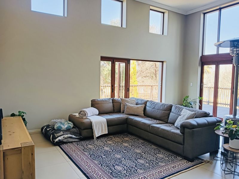 Spacious living room featuring high ceilings, clerestory windows, and large timber-framed folding doors that provide seamless access to the outdoor deck area.