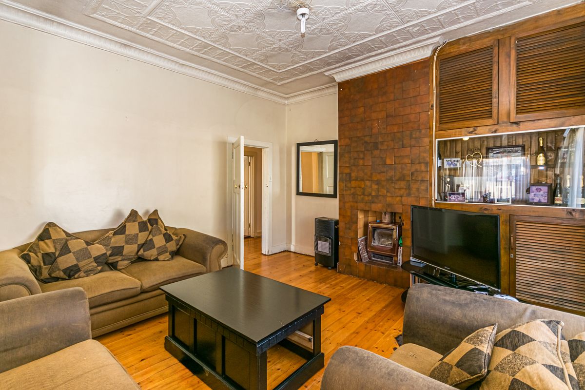 Living room featuring original pressed metal ceilings, timber flooring, and a built-in fireplace with integrated cabinetry.