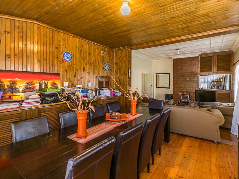 Open plan living and dining area featuring extensive timber wall paneling, a brick fireplace with a wood burning stove, and timber flooring.