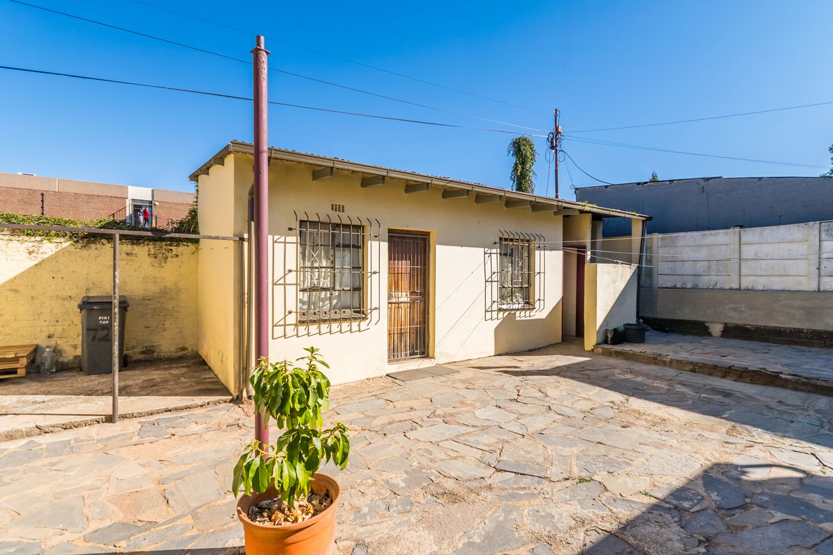 Rear exterior view of the property featuring a stone-paved courtyard, security bars on windows, and a metal security gate.
