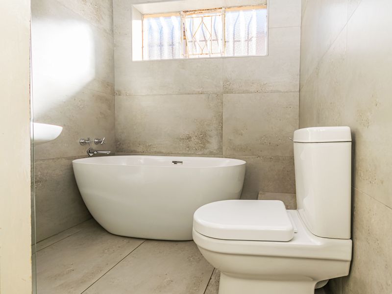 Modern bathroom featuring a sleek freestanding bathtub, contemporary toilet, and neutral large-format wall and floor tiles.