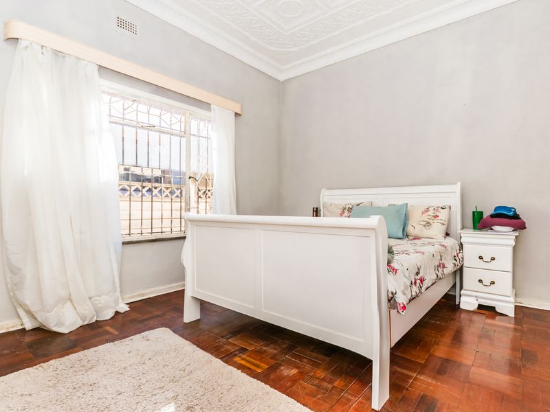 A bedroom featuring classic parquet flooring, ornate ceiling detailing, and a window fitted with security bars.