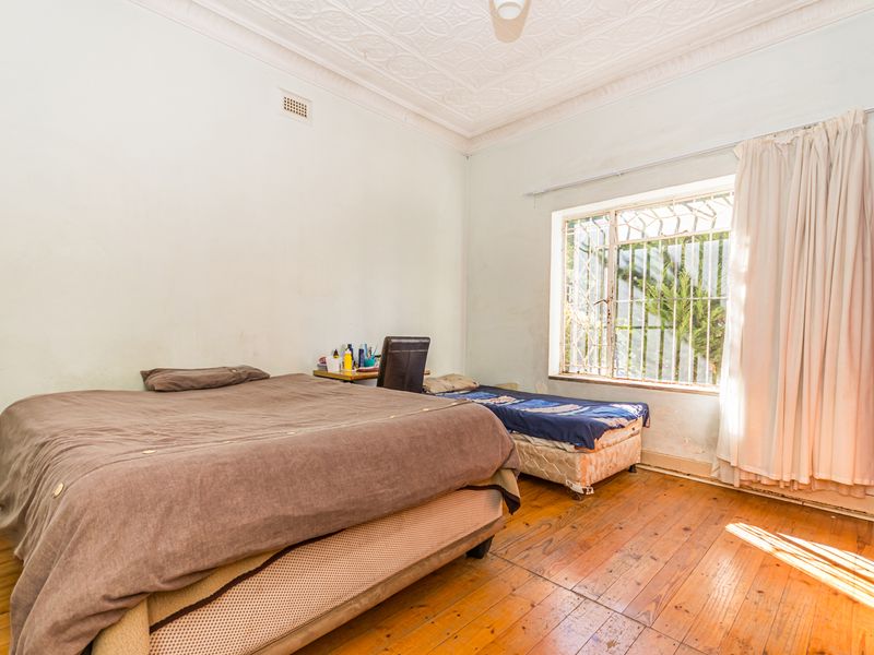 A bedroom featuring original pressed metal ceilings, timber flooring, and security bars on the window, requiring cosmetic updates to the walls and floors.