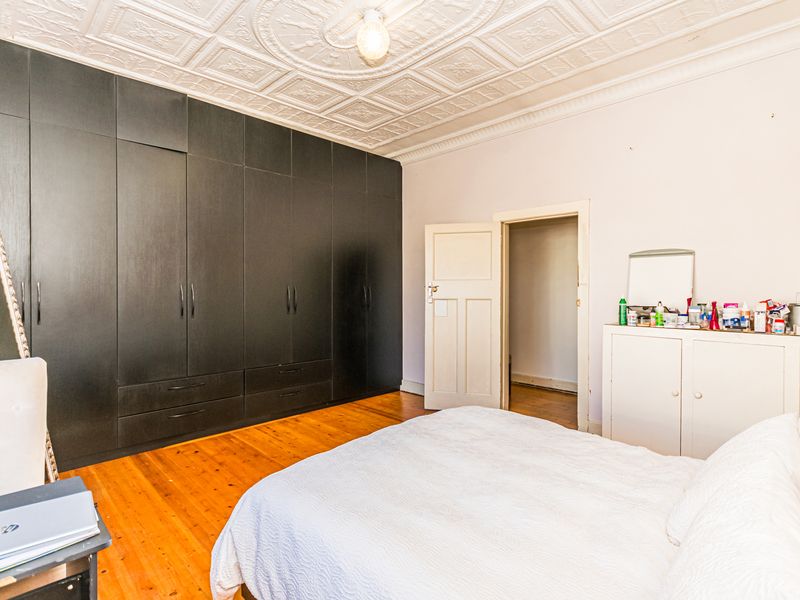 Spacious bedroom featuring classic pressed metal ceilings, polished timber flooring, and extensive floor-to-ceiling built-in cabinetry.