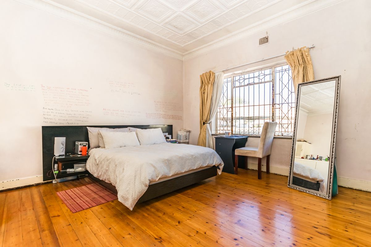 Spacious bedroom featuring original pressed metal ceilings and polished timber flooring, requiring cosmetic updates to walls and window fixtures.